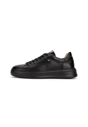 Baskets basses en cuir noir avec lacets noirs, semelle plate et détail subtil de logo métallique sur le côté, présentées en profil latéral.