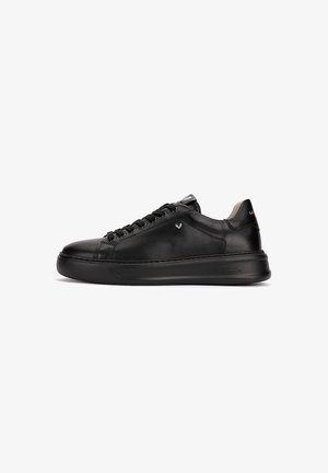 Baskets basses en cuir noir avec lacets noirs, semelle plate et détail subtil de logo métallique sur le côté, présentées en profil latéral.