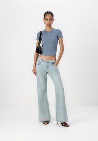 Light blue fitted t-shirt with a small red logo, paired with wide-leg light wash jeans, and black strappy heels. Small black handbag accent.