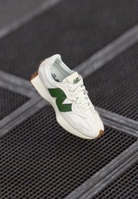 White athletic sneaker featuring a green side accent, textured fabric, and a rubber outsole. Laces are white, with a cream tongue.