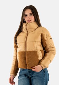 Lätt vadderad jacka i beige med en brun fleecepanel. Har hög krage, dragkedja och elastiska muddarna. Mjuk textur över hela plagget.