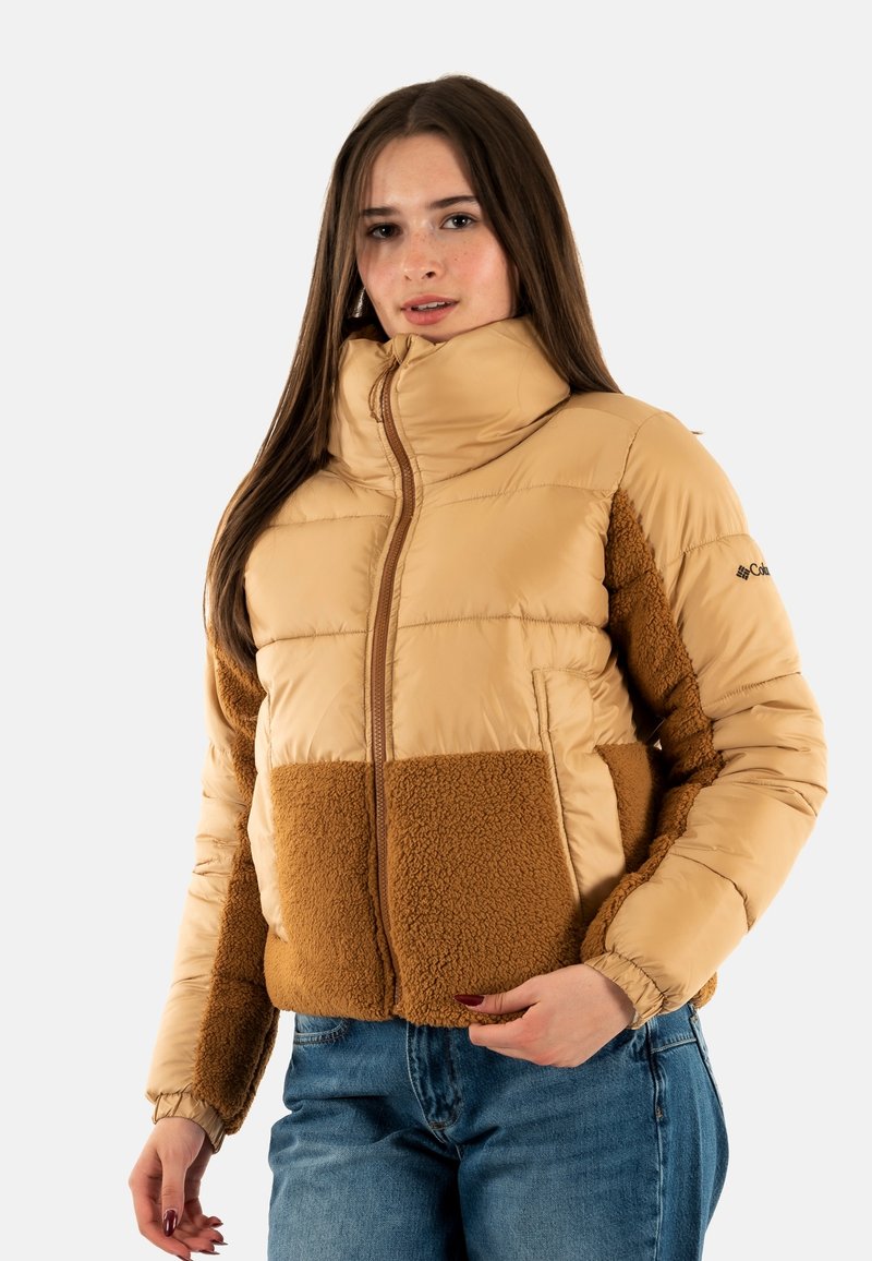 Lätt vadderad jacka i beige med en brun fleecepanel. Har hög krage, dragkedja och elastiska muddarna. Mjuk textur över hela plagget.