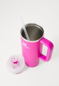 Mug de voyage en acier inoxydable rose vif avec poignée, paille réutilisable transparente à l'intérieur et couvercle en plastique rose et blanc détaché sur une surface blanche.