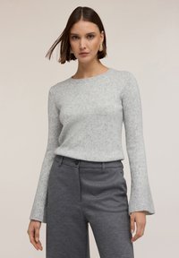 Ljust grå, texturerad tröja med rund halsringning och klockformade ärmar, kombinerad med mörkgrå skräddarsydda byxor.