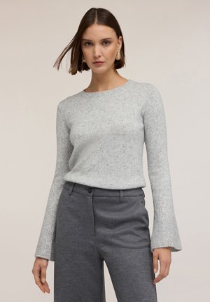 Jasnoszary, teksturowany sweter z okrągłym dekoltem i rękawami w kształcie dzwonów, zestawiony z ciemnoszarymi, dopasowanymi spodniami.
