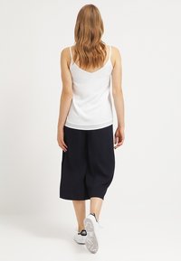 Débardeur blanc à fines bretelles, associé à des culottes noires amples arrivant au genou et des baskets blanches avec des accents noirs.