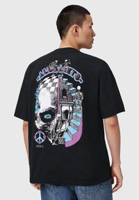 Sort t-shirt med en iøjnefaldende grafisk design, der viser et kranium, skeletter og farverige accenter. Kortærmet og afslappet pasform med rund halsudskæring.