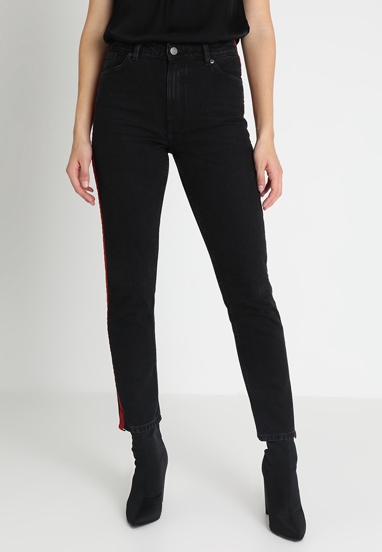 Černé džínsy s vysokým pasem, úzkého střihu, s červeným bočním pruhem a klasickým pětiokou designem. Materiál vypadá elasticky, s jemnou texturou.