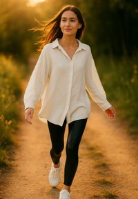 Witte blouse, zwarte leggings en witte sneakers, wandelend op een pad met gras en bloemen, zacht zonlicht op de achtergrond.