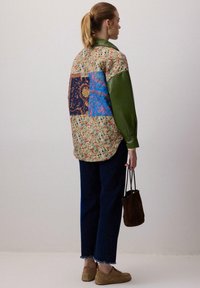 Patchwork skjorte med florale, paisley og ensfarvede grønne sektioner; afslappet pasform, knap-up stil, parret med mørke jeans og tan sko.