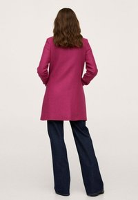 Abrigo de lana magenta con un corte entallado, mangas largas y abertura trasera, combinado con jeans oscuros de pernera acampanada y botas negras.