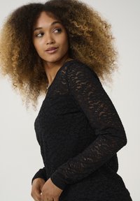 Top in pizzo nero con maniche lunghe, un motivo floreale texture e una silhouette aderente. Tessuto morbido e trasparente con scollatura rotonda.