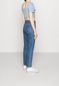 Top corto de flores azules con mangas abullonadas, combinado con jeans de cintura alta azul. Zapatillas blancas, corte recto y detalles de costura mínimos.