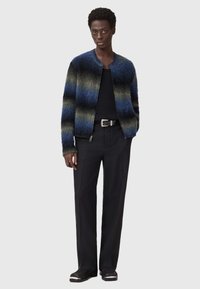 Teksturiran modro-zelena prugasta jopica iz mehkega materiala, v kombinaciji z črnimi hlačami in črno srajco, ki ima srebrni pas.