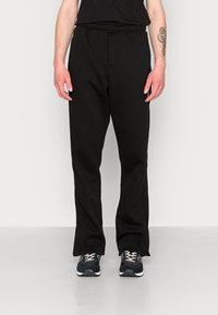 Czarne dresy wykonane z miękkiego materiału, z elastycznym paskiem w talii, prostym krojem i delikatnymi bocznymi kieszeniami. W zestawie z czarnymi butami sportowymi.