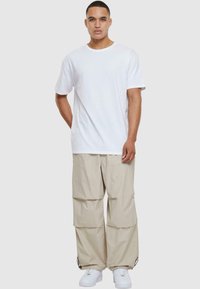 Hvid bomulds T-shirt med korte ærmer kombineret med beige cargo-bukser med folder og lynlåse ved anklerne. Båret med hvide sneakers.