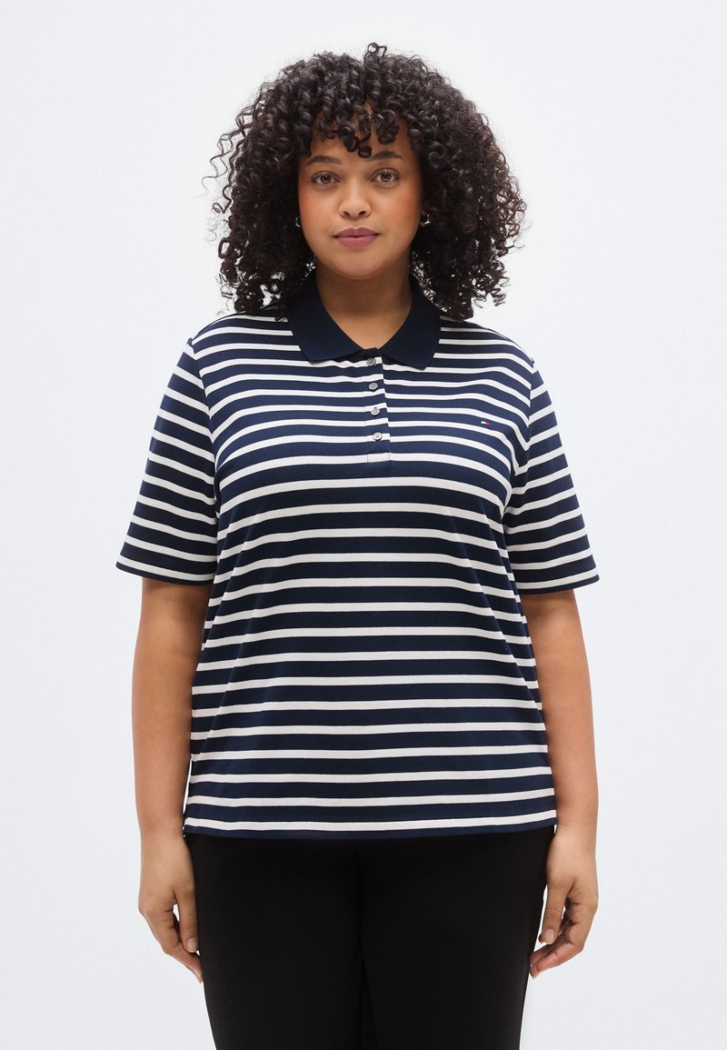 Ριγέ μπλε ναυτικό και λευκό πόλο μπλουζάκι με κοντά μανίκια, κούμπωμα με κουμπιά και γιακά. Το ύφασμα φαίνεται μαλακό και υφασμένο. Διακριτικό λογότυπο ορατό.