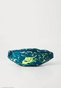 Sac banane Nike en bleu avec un motif ondulé vert et jaune. Il présente un logo jaune proéminent, une fermeture éclair et une sangle ajustable.
