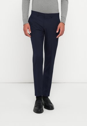 Schmale, taillierte Navy-Hose aus glattem Stoff; Slim Fit; mit Gürtelschlaufen und Fronttaschen. Kombiniert mit schwarzen Slippern und Socken.