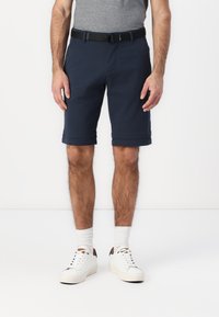 Shorts bleu marine en tissu doux, avec des ourlets roul�és, une ceinture noire, portés avec des baskets blanches et des chaussettes.