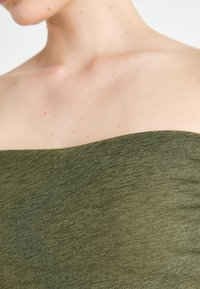 Olive rohelise värvi pealata top, millel on sujuv, tekstuuriga kangas ja sirge kaelus. Materjalil on kerge sära ja venivus.