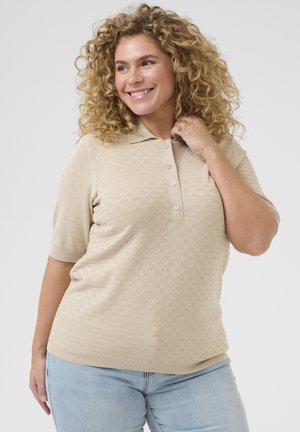 Polo shirt en tricot beige à manches courtes, présentant un motif en losanges et une patte de boutonnage. Texture douce, coupe décontractée et ourlet à côtes.