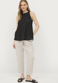 Zwarte mouwloze top met een relaxte pasvorm en een textuurfinish, gecombineerd met lichtbeige linnen broeken en zwarte slippers.