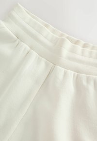 Cintura elástica blanca con tela crema fruncida debajo, mostrando detalles de textura y costuras en la prenda.