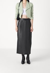 Blazer corto verde claro sobre un top corto blanco, combinado con una falda larga de cuero negra y botines negros de puntera.