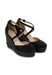Sandales compensées noires avec des brides croisées à la cheville, ornées de strass, présentant une texture tissée et un design à bout rond.
