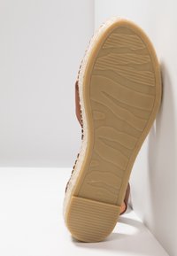 Semelle d'une sandale marron taille 37 avec une semelle extérieure en caoutchouc texturé et une semelle intermédiaire tissée style espadrille, positionnée sur un fond blanc en coin.