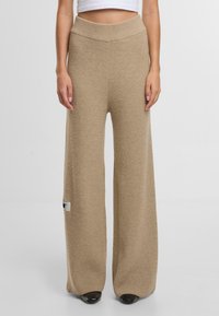 Béžové kalhoty se širokými nohavicemi z texturované pleteniny, vysokým pasem a malým logem na boku. Dlouhý a volný střih.