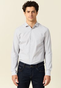 Lichtblauwe overhemd met lange mouwen met een klein stippenpatroon, button-down kraag en manchetten. Draagt bij donkere denim jeans.