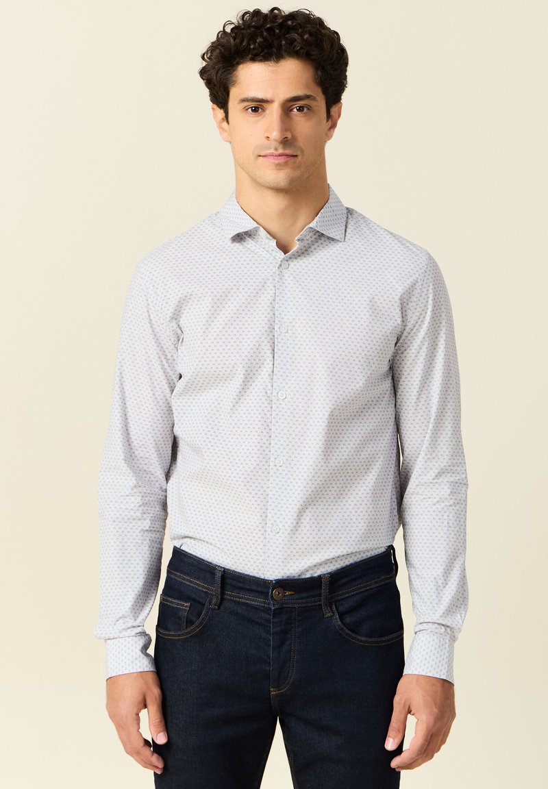 Lichtblauwe overhemd met lange mouwen met een klein stippenpatroon, button-down kraag en manchetten. Draagt bij donkere denim jeans.