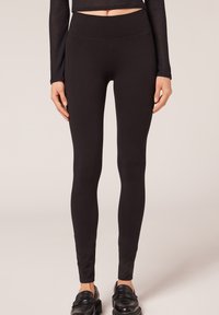 Schwarze Leggings mit hohem Bund, aus einem glatten, dehnbaren Material gefertigt. Das Design ist figurbetont mit einer nahtlosen Optik.
