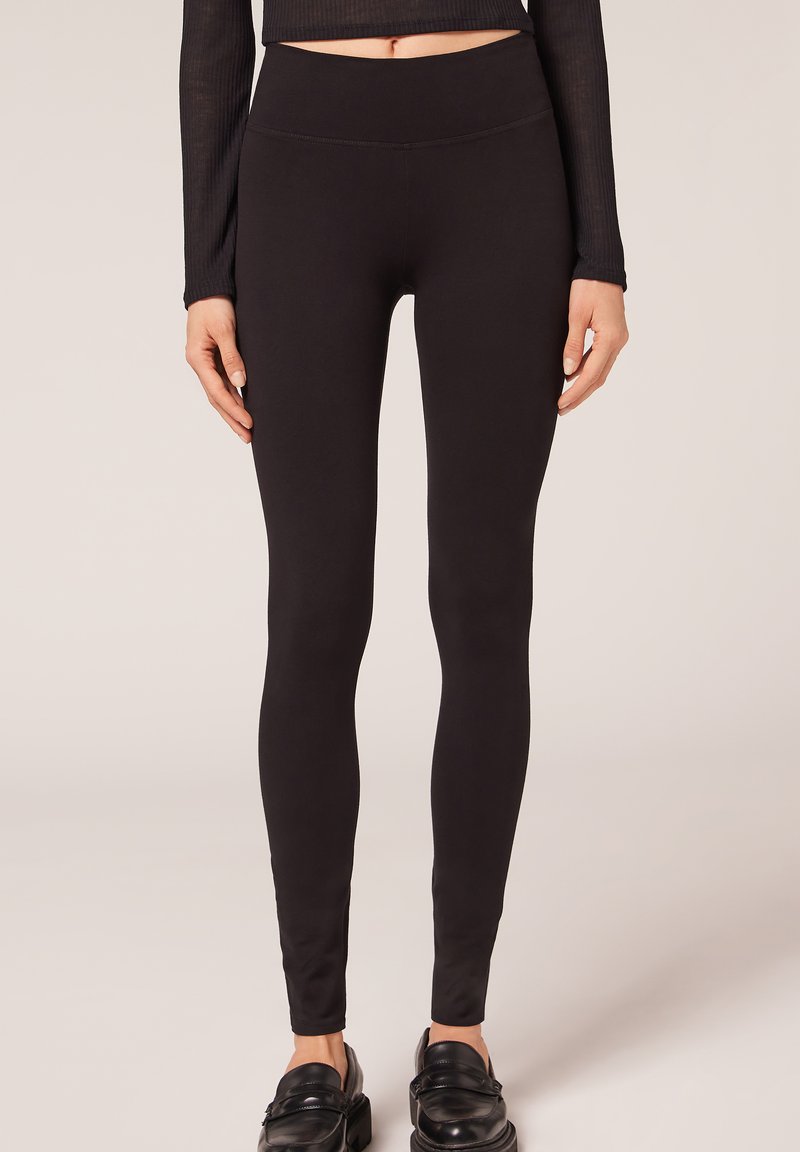 Schwarze Leggings mit hohem Bund, aus einem glatten, dehnbaren Material gefertigt. Das Design ist figurbetont mit einer nahtlosen Optik.
