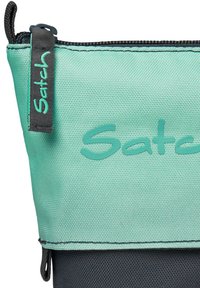 Une pochette en tissu vert menthe avec une fermeture éclair noire et une surface texturée, portant le mot "Satch" imprimé dans une couleur vert menthe assortie.