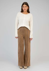 Pull en maille côtelée crème avec fermeture à boutons, accompagné de pantalons en daim marron taille haute à jambes larges et de chaussures à enfiler beiges.