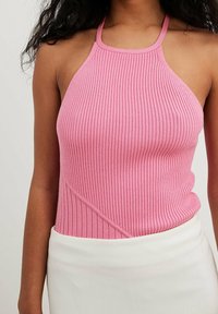 Roze geribbelde haltertop met een getailleerde pasvorm, voorzien van een diagonaal patroon en een gladde textuur, gecombineerd met een witte rok.