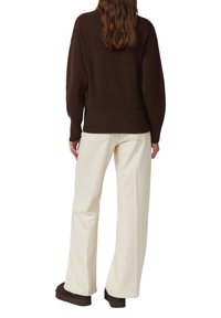 Brauner übergroßer Pullover mit geripptem Saum, kombiniert mit cremefarbenen, weit geschnittenen Hosen. Strukturierte Lagen und lockere Passform. Braune Schuhe vervollständigen den Look.