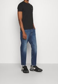 Camiseta negra de manga corta, jeans de mezclilla azules y zapatos negros con detalles blancos. Conjunto casual centrado en la comodidad y el ajuste.