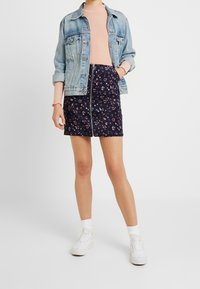 Jeansjacka över en rosa ribbad tröja, i kombination med en marinblå blommönstrad kjol. Vita sneakers och strumpor fulländar outfiten.