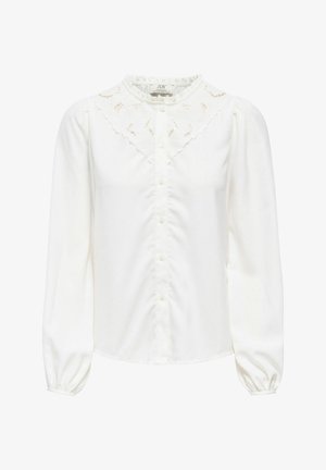 Blouse blanche à manches longues avec fermeture à boutons, dentelle sur le haut de la poitrine, et poignets et encolure froncés.