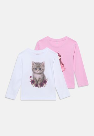 Deux chemises pour enfants à manches longues, une blanche avec un motif de chaton et de fleurs, une rose avec une illustration d'une fille portant une couronne.