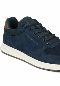 Navy blue Tommy Hilfiger sneaker with brown heel patch, black laces, perforated side, and white sole with brown tread.