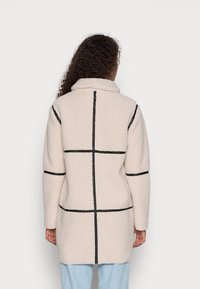 Lys beige, teksturert teddy-kåpe med svart rutemønster, bred krage og lange ermer. Bakfra vises designdetaljene.