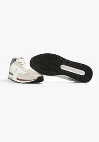 Scarpe da ginnastica bianche con accenti grigi, tessuto testurizzato, suole decorate e un logo con teschio e ossa incrociate sul lato.