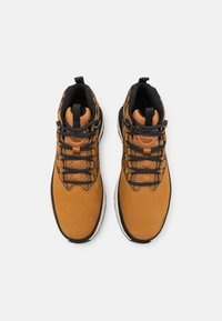 Braune Leder-Mid-Top-Schuhe mit schwarzen Akzenten, gemusterten Schnürsenkeln und einer weißen Sohle. Eigenschaften wie ein gepolsterter Kragen und strukturierte Oberflächendetails.