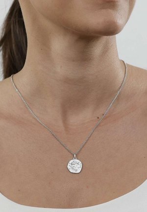 Silver chain necklace with a round, textured pendant worn on a woman's neck against a white top and light gray background.