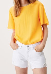 Top giallo a maniche corte con texture e orlo scallop, abbinato a shorts di denim bianchi con bordi sfilacciati e tasche frontali.